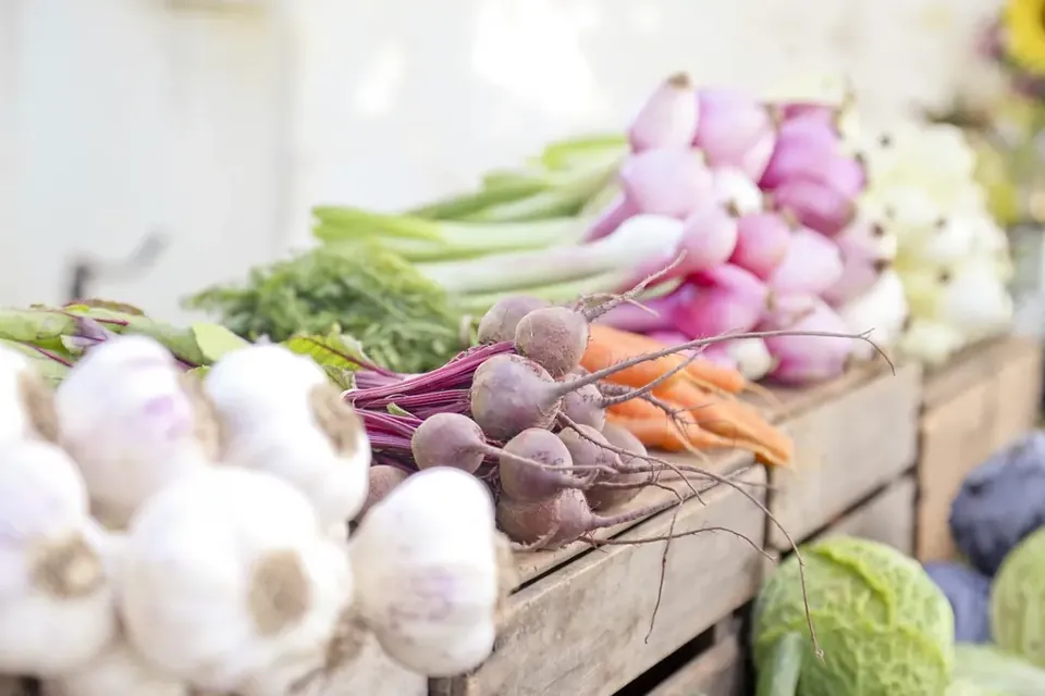 Garlic bulbs, beetroot, spring onions and cabbage displayed in wooden crates at a market stall