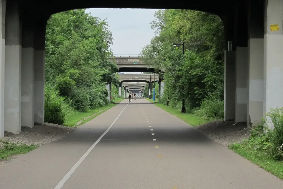 A wide, tree-lined bike and walking path in a sunken former rail corridor passing under a series of bridges