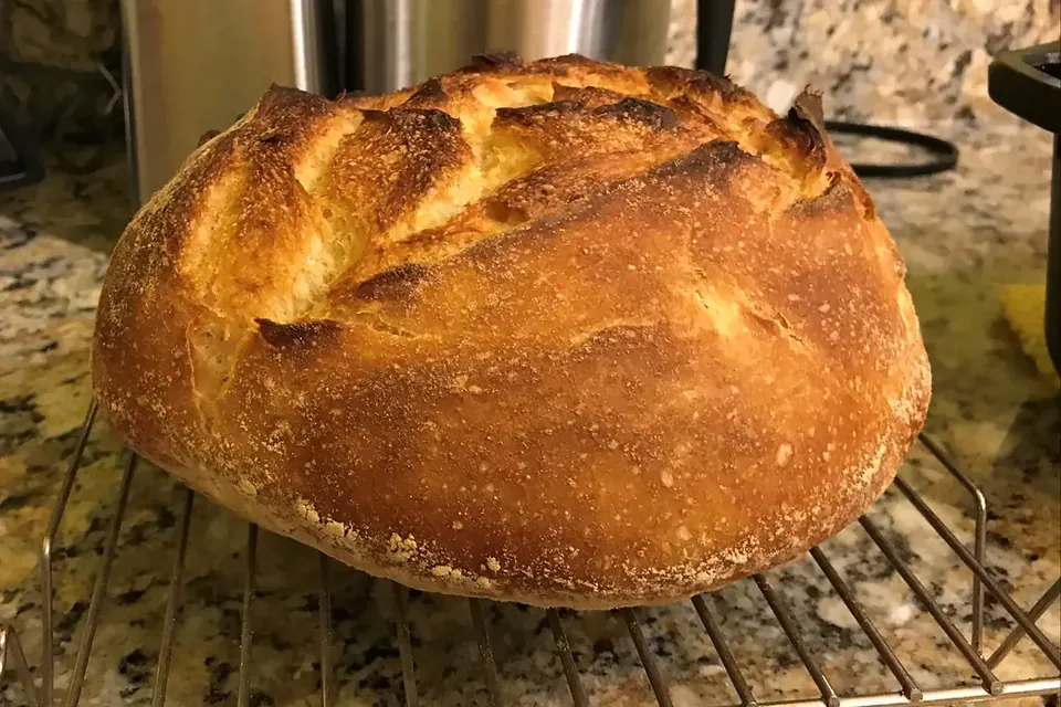 A round, golden sourdough loaf with a crackled crust cooling on a wire rack in a home kitchen