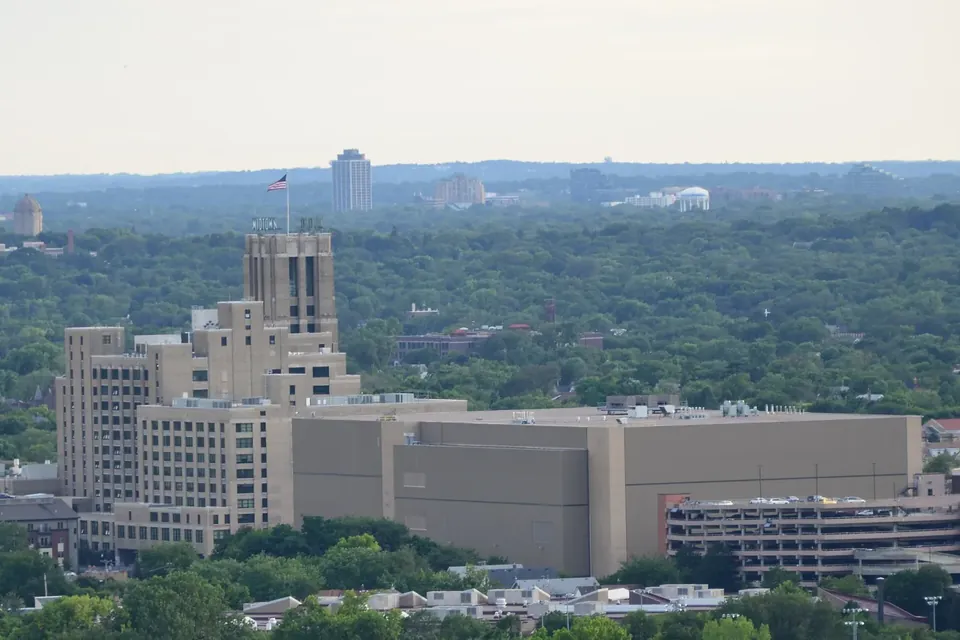 A large brick and concrete building with a central tower seen from above, surrounded by trees and the low roofs of south Minneapolis