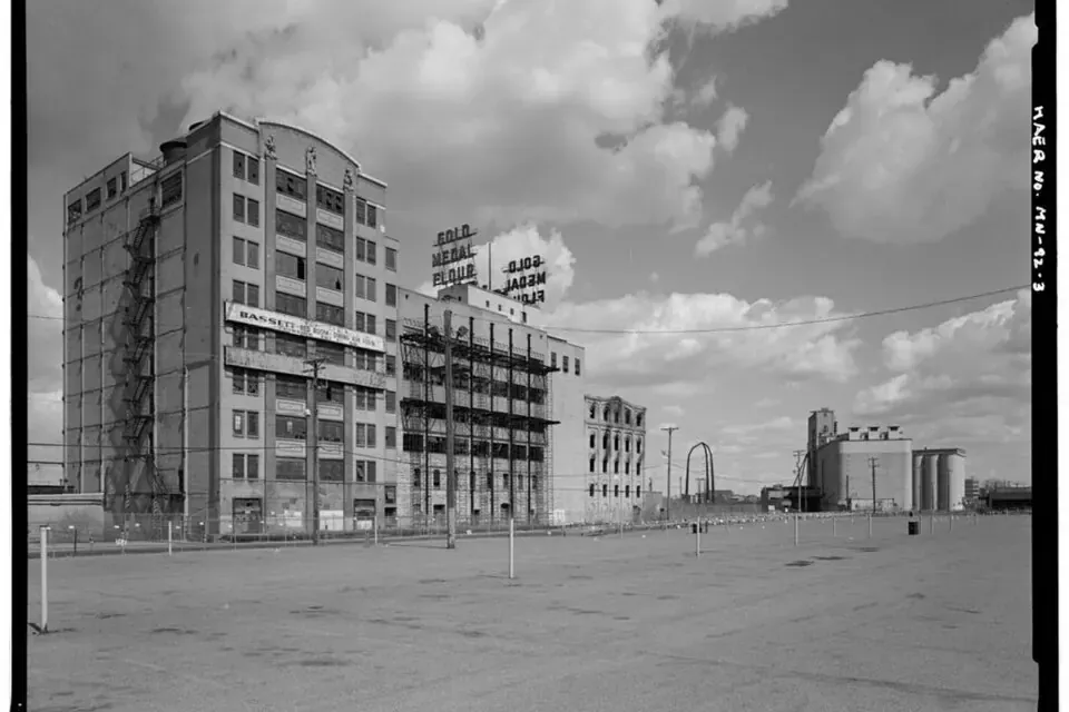 Black and white documentary photograph of tall concrete grain elevators and mill buildings beside the Mississippi