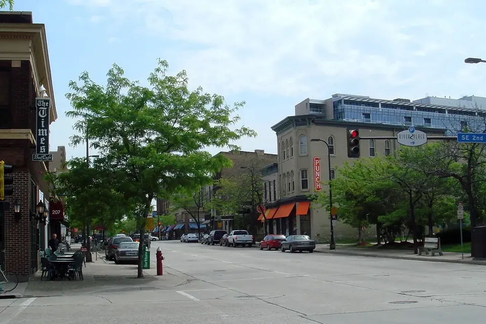 A street corner in Northeast Minneapolis with low brick commercial buildings, trees and a traffic signal