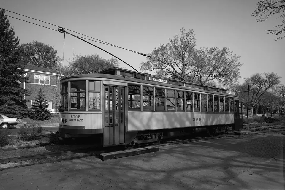 Black and white photograph of a vintage wooden streetcar on its track beside trees and a station shelter