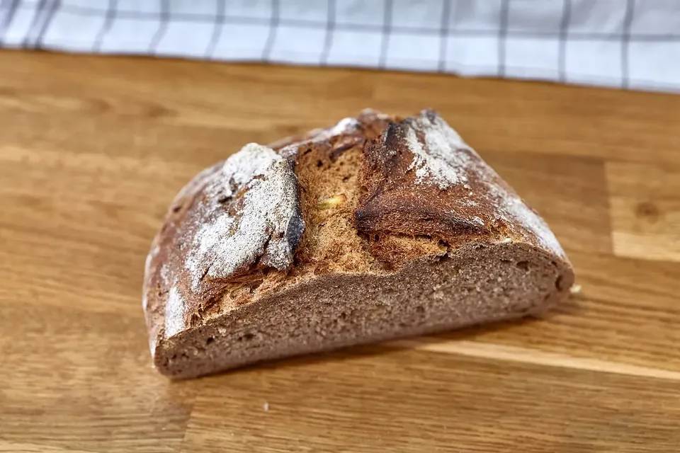 A dark rye loaf cut open on a board, showing a dense, moist crumb
