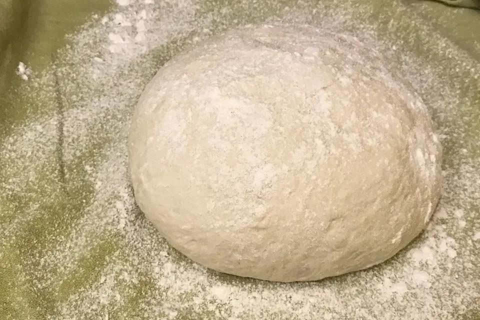 A smooth, round ball of bread dough resting on a floured surface